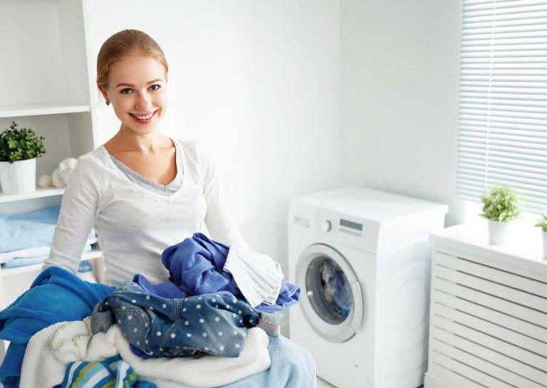 A smiling woman holding a pile of laundry beside a washing machine