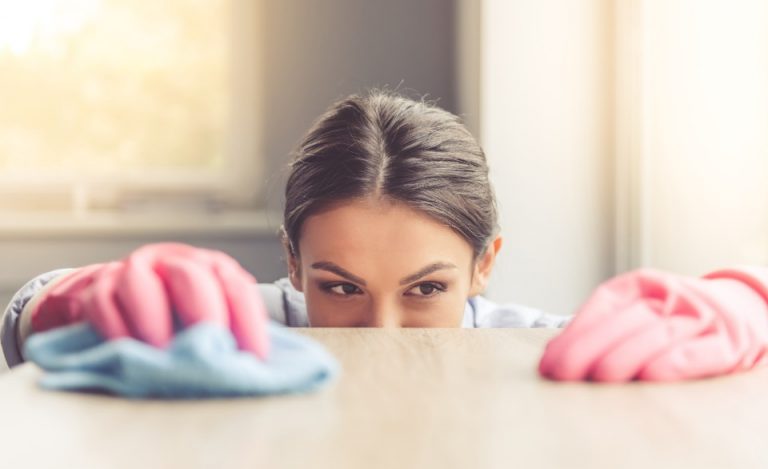 A woman peeking over a table, with pink cleaning gloves and a cloth in front of her